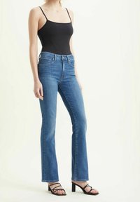 Body de tirantes negros tipo espagueti combinado con vaqueros acampanados azul claro. Los vaqueros presentan un diseño clásico de cinco bolsillos y un ligero desgaste.