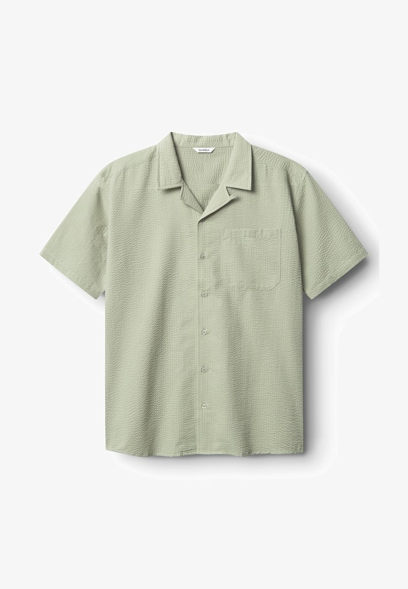 Majica s kratkimi rokavi v svetlo zeleni barvi, teksturiranega blaga. Ima razprt ovratnik, sprednji žep in zapenjanje na gumbe. Enostavna zasnova brez vzorcev.
