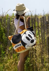 Bolso grande de tela con un diseño en negro y naranja que presenta una cara prominente de Mickey Mouse y patrones de dibujos animados repetidos. Asa de cuerda.
