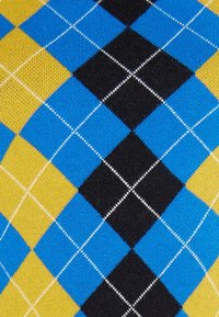 Dziana tkanina z geometrycznym wzorem argyle w odcieniach niebieskiego, czarnego, żółtego i białego, z kontrastującymi kształtami diamentów i delikatną teksturą.