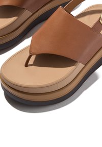 Bruine leren sandalen met een brede teenband en een gestapelde plateauzool, voorzien van een tan gekleurde middenzool en een donkere buitenzool voor extra contrast.