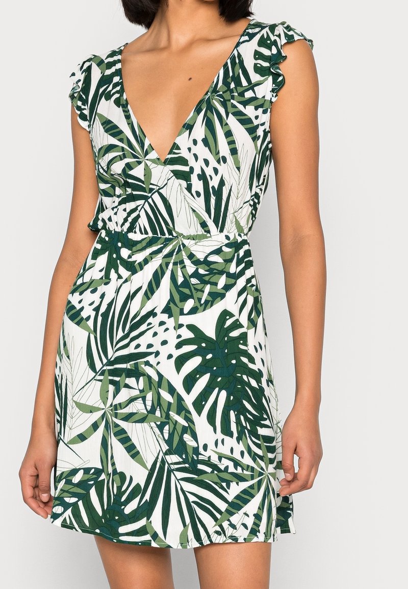 Robe portefeuille à manches courtes avec un motif de feuillage vert sur fond blanc, dotée d'un décolleté en V profond et de manches à volants.