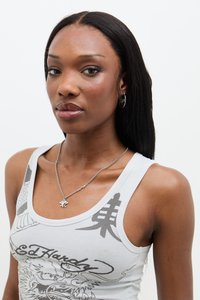 Grå grafisk tanktop med svart drage-design og asiatiske tegn; sølvhalskjede med en liten logo-pendant; modellen har langt, rett hår.