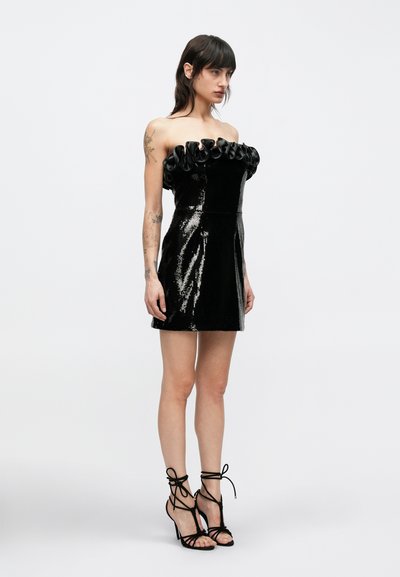 Melna mini vakarkleita bez lencītēm ar svārkiem no fliteriem, rievotu kakla izgriezumu, pieguļošu korseti un izplatu svārku. Valda ar melnām augstpapēžu sandales ar šņorēm.