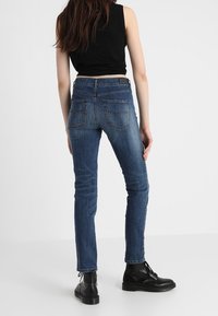 Indigo modré slim-fit džíny s polovičním pasem, pěti kapsami a jemnými švy, spárované s černými kotníkovými botami.