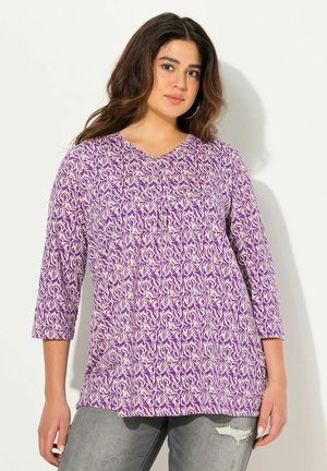 Blouse violette à manches trois-quarts, avec un motif floral crème, décolleté en V, détails froncés et coupe décontractée.