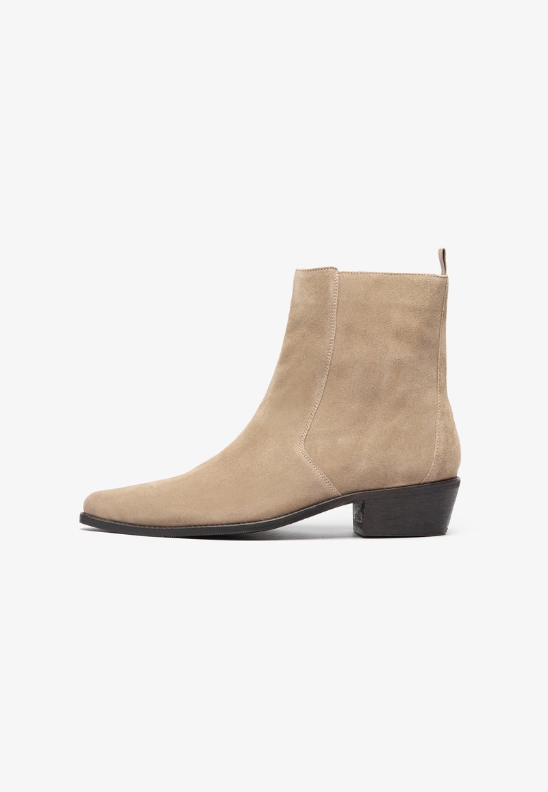 Botín de ante beige hasta el tobillo con punta afilada, diseño minimalista y un tacón bajo apilado. Cuenta con una lengüeta en la parte trasera para facilitar su uso.