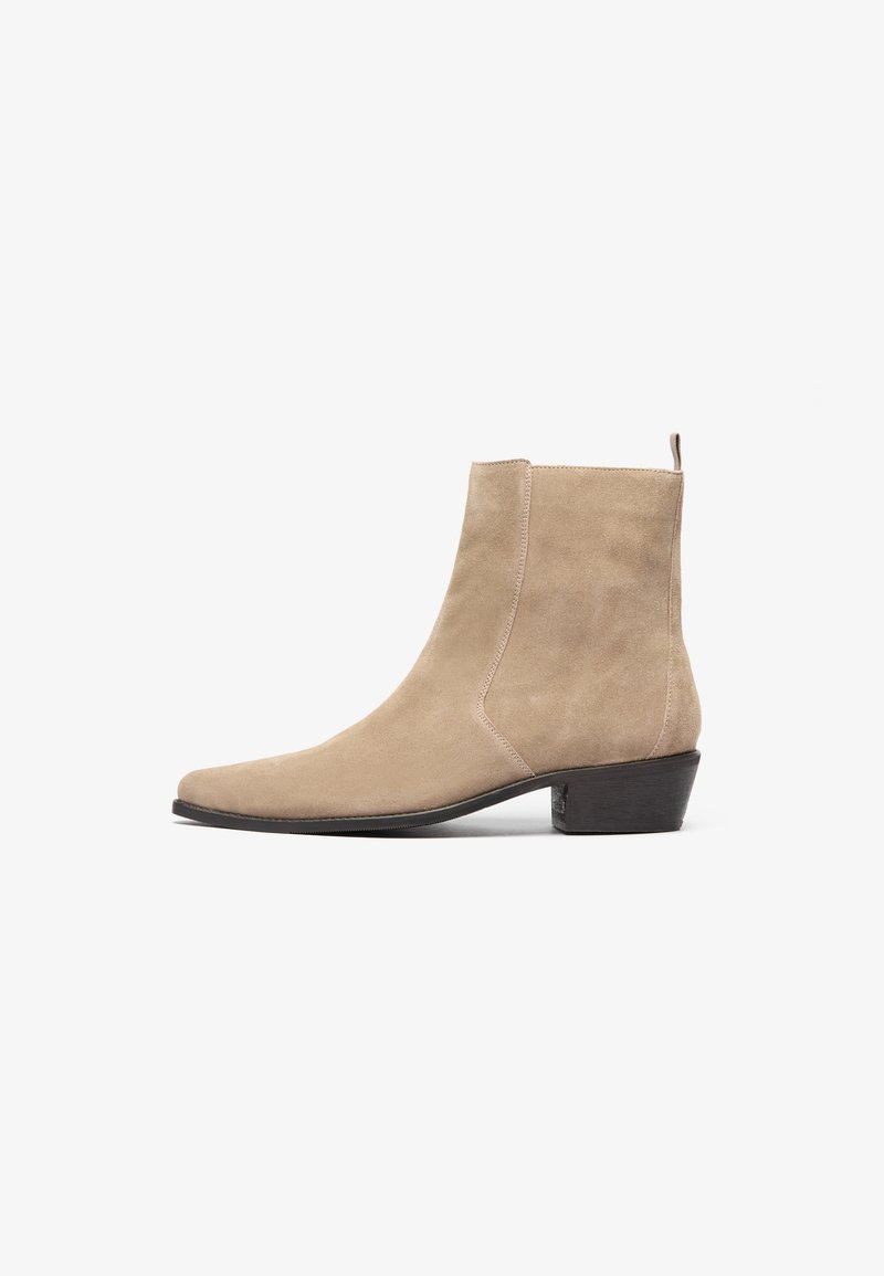 Beige suede ankle boot with a pointed toe, minimalistic design, and a low stacked heel. Features a pull tab at the back for easy wear.