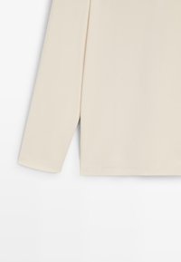 Beżowa bluzka z długim rękawem wykonana z miękkiego materiału, o luźnym kroju, z okrągłym dekoltem i subtelnymi rozcięciami po bokach przy dole.