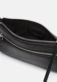 Borsetta in pelle nera con cerniera argentata, texture liscia e etichetta interna. Accompagnata da una sottile tracolla in pelle. Design compatto.