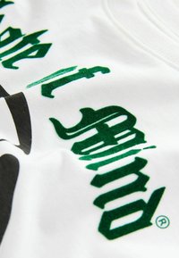 Valge puuvillane t-särk, millel on rohelise sametise tekstuuriga lettering ja mustad graafilised elemendid, pehme ja sujuva koe viimistlusega.