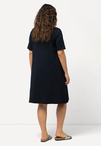 Navy modro zkrácené šaty s volným střihem, do délky kolen, vyrobené z měkké látky. V kombinaci s pohodlnými šedými sandály s korkovou podrážkou.