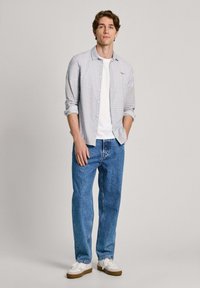 Ljust blå skjorta med mönster, vit t-shirt under, blå denimjeans och vita sneakers med bruna sulor.