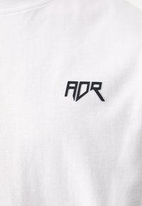 White cotton T-shirt with a textured black "ADR" logo on the left chest area. The fabric features a fine ribbed texture.