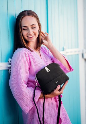 Schwarze Lederhandtasche mit strukturierter Oberfläche, runder Form, silbernem Zubehör und abnehmbarem Schulterriemen, vor einem blauen Hintergrund gehalten.