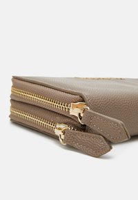 Geantă din piele texturată maro, cu două fermoare aurii și accente superioare, având o finisare netedă și o formă rectangulară.
