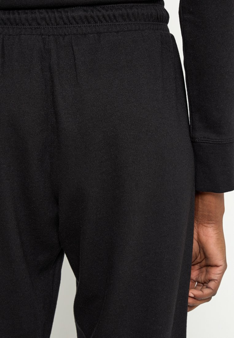 Czarne bawełniane spodnie dresowe z elastycznym pasem, charakteryzujące się gładką fakturą i dopasowanym krojem, widoczne częściowo od pasa w dół.