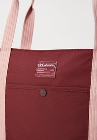 Bordeaux stoffveske med teksturerte rosa stropper. Har et Columbia-logo-merking og en frontlomme med knappelukking.