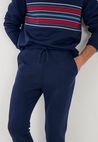 Marineblauwe sweatshirt met een gestreept patroon van rood, lichtblauw en wit. Gecombineerd met bijpassende marineblauwe joggers met een trekkoord in de taille en een zachte textuur.