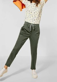 Olive green pants with a drawstring waist and side pockets, paired with a floral print shirt and white sneakers. Smooth fabric, casual fit.