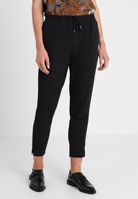 Czarne spodnie z elastycznym pasem, z kieszeniami po bokach, slim fit, długość do kostek, gładka tekstura materiału, zestawione z czarnymi butami perforowanymi.