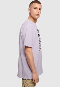 Lys lavendel oversized t-skjorte med korte ermer, med svart grafisk tekst på fronten. Laget av myk, lett bomull.
