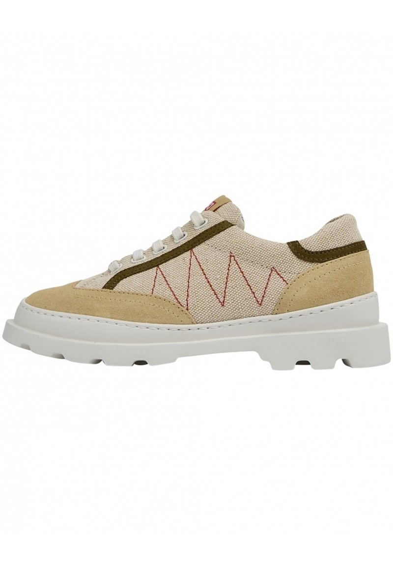 Beige and tan sneaker with a textured canvas upper, contrasting olive green accents, red zigzag stitching, and a thick white rubber sole.