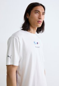 Hvid bomulds t-shirt med BMW Motorsport logo på forsiden og et gråt Puma logo på venstre ærme. Casual pasform med korte ærmer.