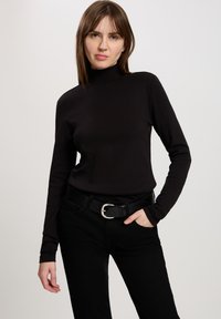 Czarny długi rękaw turtleneck o dopasowanym kroju, wykonany z gładkiego materiału. W połączeniu z czarnymi spodniami z wysokim stanem i błyszczącym skórzanym paskiem.