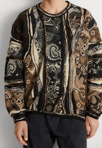 Sweter z dzianiny, łączący odcienie brązu, czerni i kremu, z geometrycznymi i abstrakcyjnymi wzorami. Lekki, z okrągłym dekoltem i ściągaczem na dole.