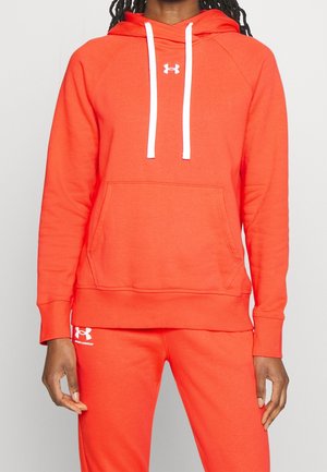 Person trägt leuchtend orangefarbenen Under Armour Hoodie mit weißen Kordeln und passende orangefarbene Jogginghose.