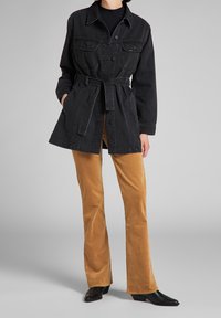 Svart denimjacka med långa ärmar, bälte och bröstfickor, i kombination med beiga kordflandsbyxor med utsvängda ben och svarta ankelskor.