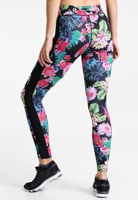 Leggings fleuris avec un fond noir, motifs de plantes en rose vif, vert et bleu, avec des panneaux latéraux noirs et une taille haute.