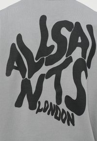 Szürke pamut póló, amelynek hátulján nagy fekete grafikus szöveg található, amely "ALLSAINTS LONDON" felirattal van ellátva, absztrakt, hullámos stílusban.