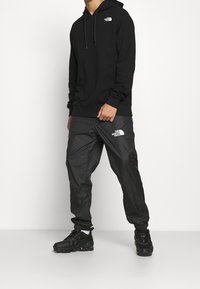 Black hoodie and grey windbreaker pants, both featuring The North Face logo. Textured fabric, casual design, and fitted, elastic cuffs on pants.