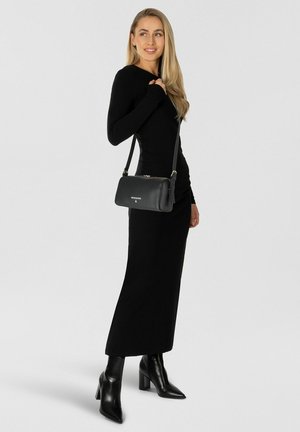 Mujer con un vestido negro ajustado de manga larga, botas negras de tacón y un bolso cruzado de cuero negro en el hombro.