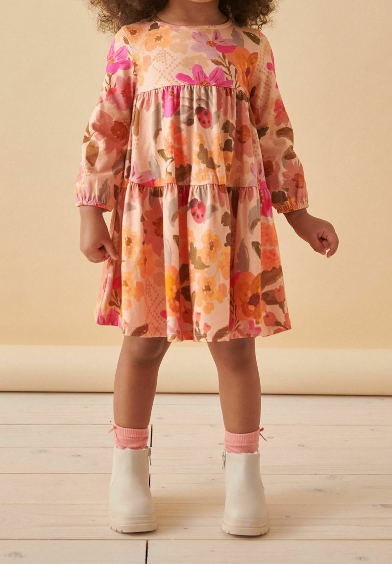 Robe fleurie aux tons roses et orange avec manches longues, taille froncée, jupe à volants et bottines blanches avec chaussettes roses.