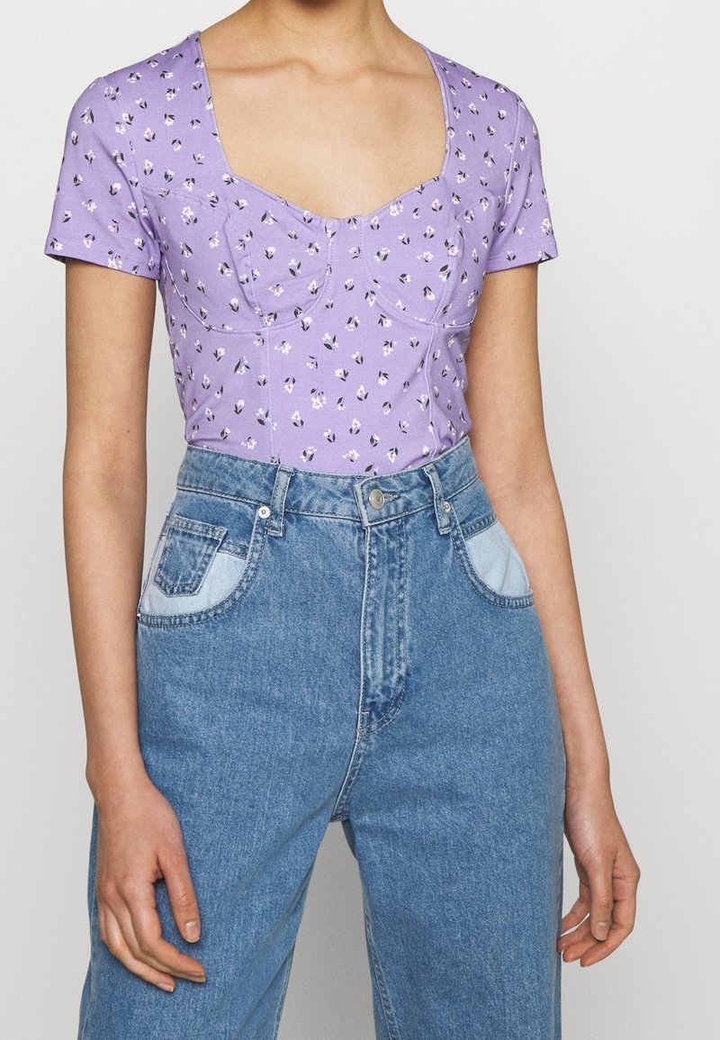 Lila kortärmad topp med blommönster, med fyrkantig halsringning och figurnära överdel, kombinerad med ljusblå hög midjejeans i denim.