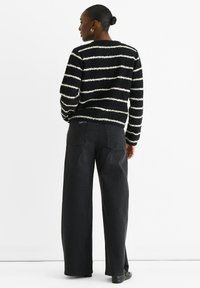 Schwarzer gestreifter Pullover mit weißer, flauschiger Textur, kombiniert mit hochgeschnittenen, schwarzen weit geschnittenen Jeans. Einfaches Design, dezente Akzente, keine sichtbaren Logos.