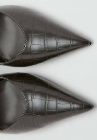 Donkerbruine, getextureerde leren pumps met een spitse neus, voorzien van een krokodillenpatroon en een gladde, semi-glanzende afwerking. Open zijkanten zorgen voor betere ademhaling.