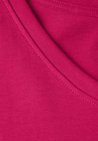 Fuchsian tyg med ribbad textur och synlig sömnad. Bilden fokuserar på den kurviga kanten och den släta ytan vid halslinningen.