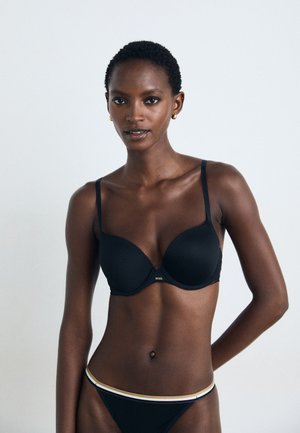 Black padded bra with adjustable straps, smooth texture, and subtle lace trim. Paired with a black bikini featuring a gold-accented waistband.