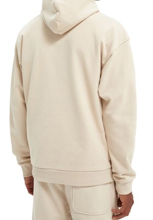 Sweat à capuche beige avec une coupe décontractée. Fabriqué en tissu doux, présentant des poignets côtelés, une ceinture côtelée et une poche kangourou à l'avant.