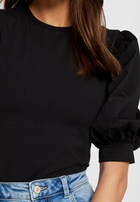 Černé bavlněné tričko s krátkými nabíranými rukávy, kulatým výstřihem a přiléhavým trupem, spárované s džínovými šortkami s vysokým pasem.