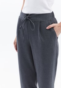 Grijze, lichte broek met een elastische tailleband, zijzakken en een gladde textuur. Het geplooide ontwerp voegt dimensie toe aan de stof.