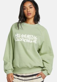 Lichtgroene sweatshirt met een ronde hals, ribbels aan de mouwen en onderrand. Bevat vetgedrukte witte tekst en bloemaccenten op de voorkant. Zachte stoftextuur.