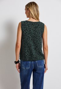 Zelená bezrukávová blůza s černým leopardím vzorem, s klíčovou dírkou na zádech. V kombinaci s světle modrými džínami. Hladká textura látky.