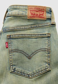 Ξεθωριασμένο μπλε τζιν με χαρακτηριστικό καμπύλο πίσω τσέπη, πορτοκαλί ραφές και καφέ δερμάτινη ετικέτα με το λογότυπο της μάρκας.