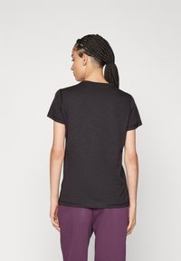 T-shirt noir avec un col rond et des manches courtes. Le tissu semble léger avec une texture lisse. Associé avec des pantalons violets.