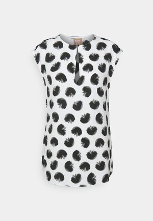 Witte mouwloze blouse met zwarte abstracte cirkelpatronen en een kleine open bies aan de voorkant onder de ronde halslijn.